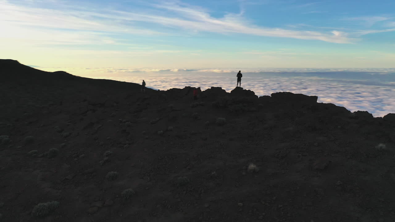 Three hikers standing on a cliff below the Pico de Teide mountain on Canary Islands and watching the sunset over the valley covered with a heavy cloud inversion. Hikers watching a mountain sunset 4K.