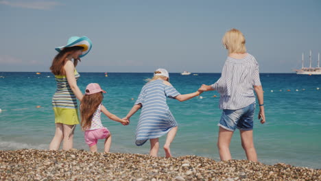 las chicas jóvenes con sus hijos pequeños se divierten en la costa saltan sobre las olas disfrutan del descanso