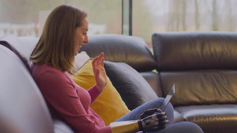 woman with prosthetic arm and hand at home making video call on laptop