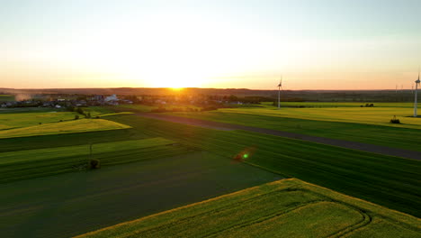 Vista-Aérea-De-Un-Campo-Verde-Y-Una-Turbina-Eólica-Al-Atardecer