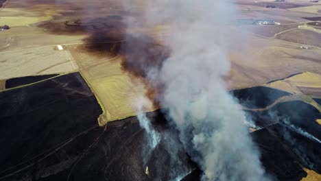Aerial-view-of-large-smoke-cloud-and-prairie-burning-surrounded-by-farmland