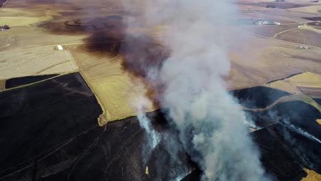 Vista-Aérea-De-Una-Gran-Nube-De-Humo-Y-Praderas-En-Llamas-Rodeadas-De-Tierras-De-Cultivo