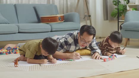 full body of asian father and sons lying on the floor in the room with plastic toy brick. drawing, talking, playing together at home