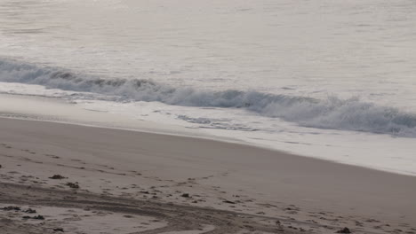 Panorámica-A-Lo-Largo-De-Una-Playa-De-Arena-Mientras-Las-Olas-Rompen-En-La-Orilla-Durante-La-Marea-Alta