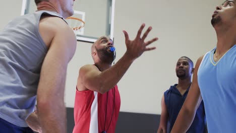 diverse male basketball coach with whistle ball and players start game at indoor court, slow motion