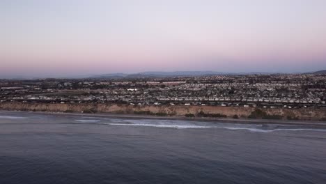 a beautiful aerial drone shot, flying towards the coast with a view of a town, the horizon, and mountains, carlsbad state beach - california