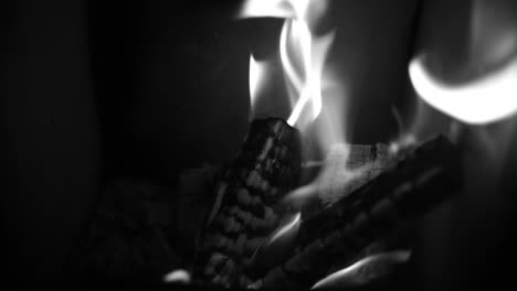 black and white closeup view of burning logs inside home fireplace with crackling flames in slow motion.