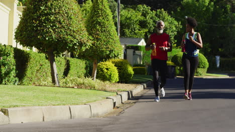 pareja de ancianos afroamericanos haciendo ejercicio al aire libre corriendo en una carretera verde soleada
