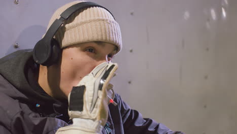 close-up of athlete wearing headphones smoking with a focused expression, the scene captures a calm and introspective moment against a metallic background