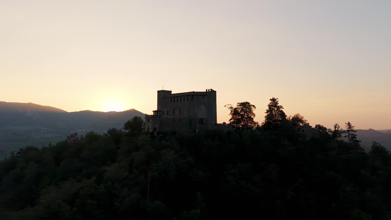 Vista drone del castello medievale Dal Verme in silhouette su una collina al tramonto a Zavattarello, Italia. Orbita aerea, spazio per il testo.
