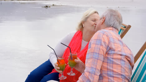 Side-view-of-old-caucasian-senior-couple-kissing-each-other-and-drinking-cocktail-at-beach-4k