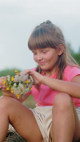 la niña se sienta en una bola de heno cubriendo juguetón la cara con flores mientras el hermano menor se ríe de ella, un sombrero de sol descansa a su lado mientras disfrutan de un momento alegre en el campo abierto