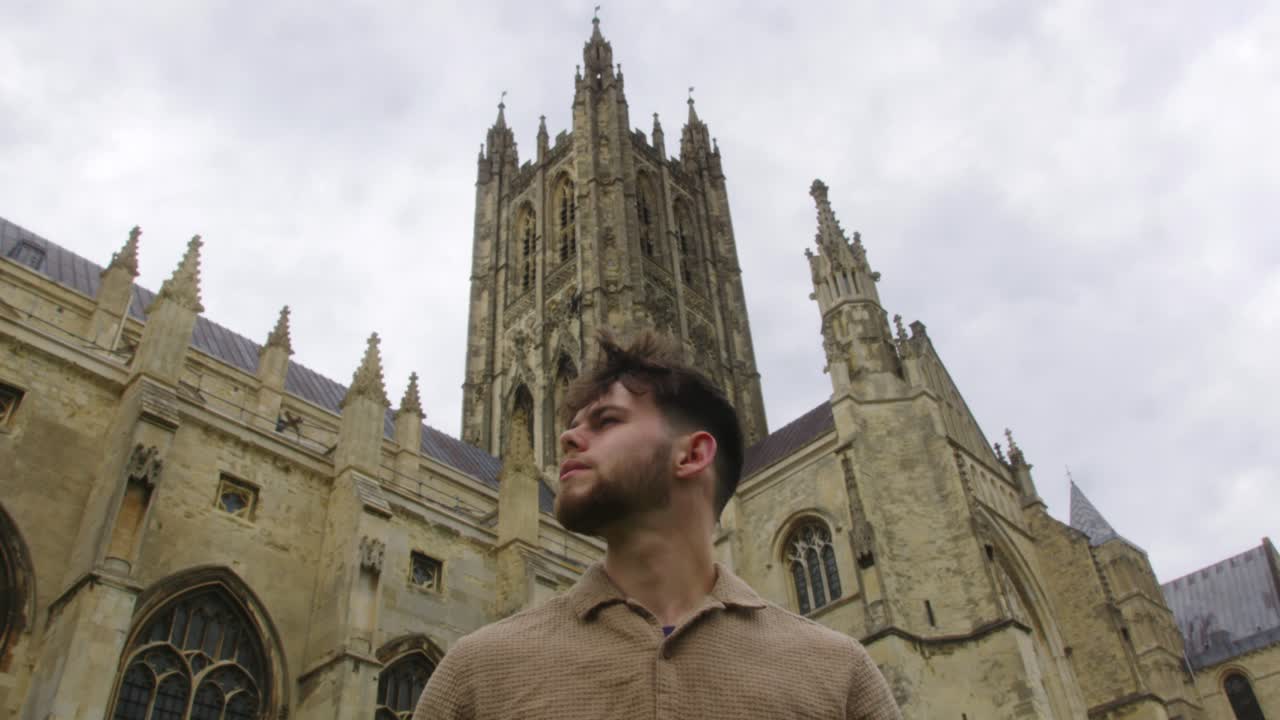 Static wide shot of a Young Man Looking Around and Walking Away in front of historic Canterbury Cathedral in Kent, England