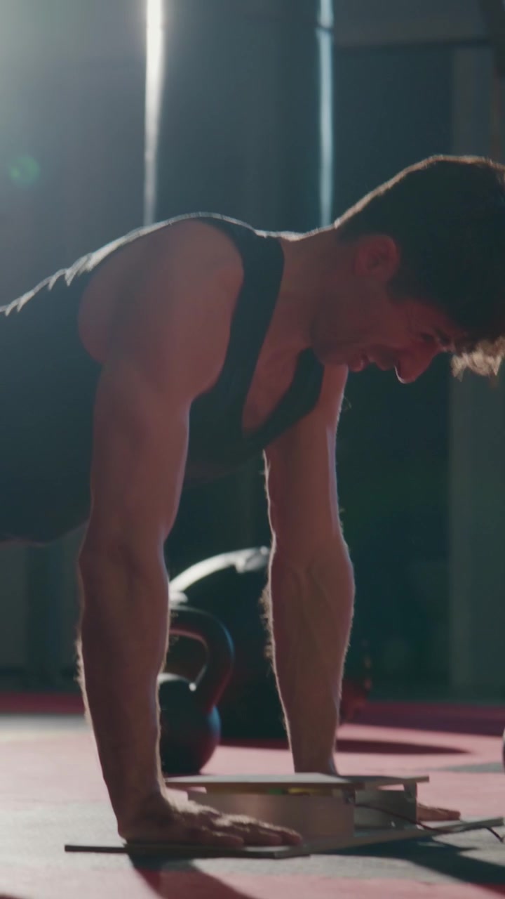 Man performs push-ups on red mat. Muscular arms show strength and focus. Sunlight highlights his determination. Ideal for fitness, workout, or motivation projects