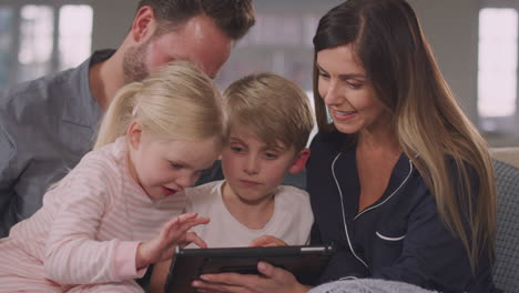 smiling family in pyjamas sitting on sofa having fun using digital tablet together