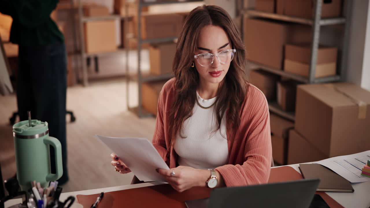 Young Woman Checking Business Documents at Desk in Warehouse Office