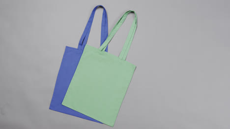 Close-up-of-blue-and-green-bags-on-grey-background,-with-copy-space,-slow-motion