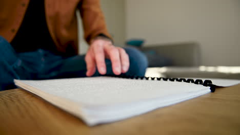 close up of an unrecognizable blind man reading a braille book while sitting on the sofa at home 1