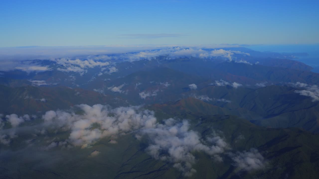 una perspectiva aérea de nubes flotando sobre un paisaje verde y montañoso durante el día