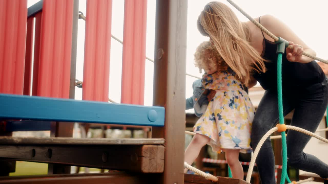 Mother and little daughter having fun on playground jungle gym