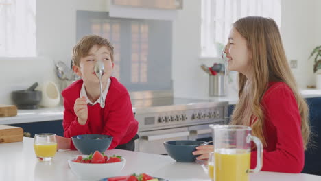 brother and sister wearing school uniform in kitchen have fun hanging spoon from nose at breakfast