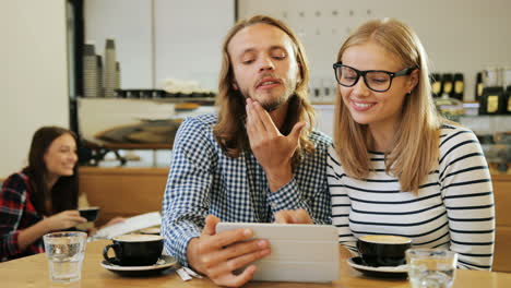 caucasian happy friends making a video call using a tablet sitting at a table in a cafe