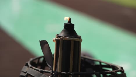 lit torch standing next to a pool, softly glowing in the daylight