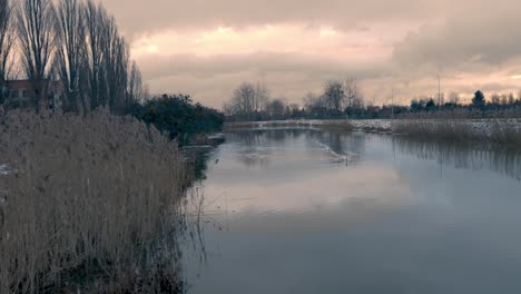 panning-nature-shot-lake-and-trees-all-around,-reflections-on-the-water-and-cloudy-moody-weather