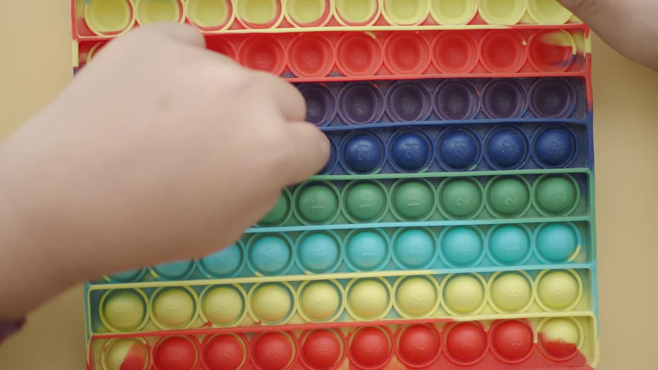 Child's Hand Playing with Colorful Pop It Fidget Toy