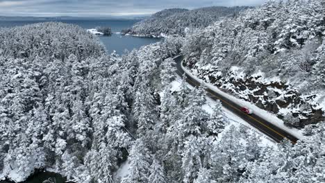 drone shot of a red truck driving through a winter wonderland with the ocean off in the distance