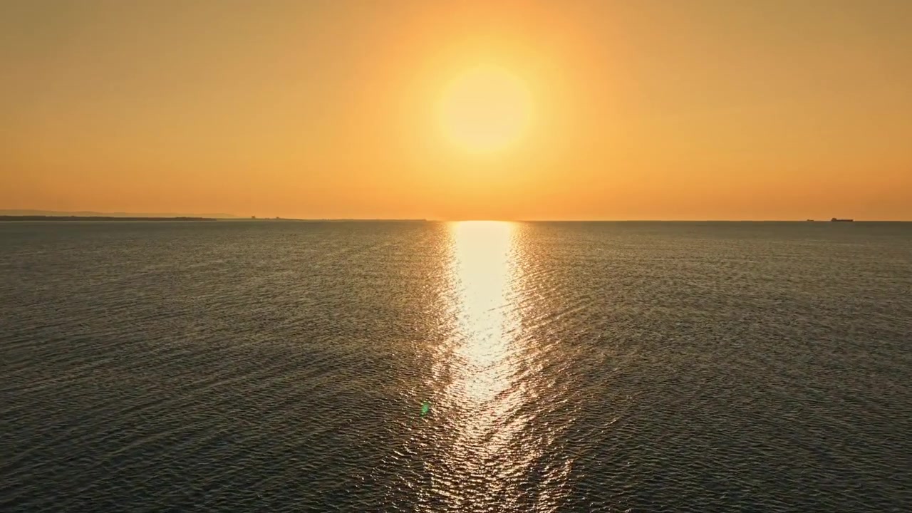 Sunset over the ocean with ships in the distance and a smooth water surface reflecting the light