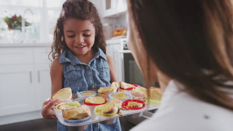 Happy-young-girl-walks-into-focus-and-presents-the-cakes-she’s-made-to-her-mum,-over-shoulder-view