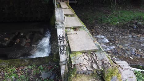 japanese characters on edge of walkway post bridge crossing above serene flowing brook stream