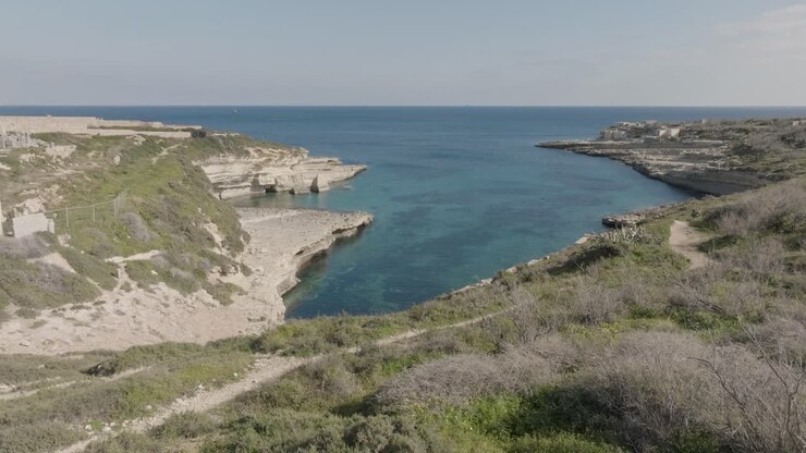 Ripresa aerea con drone sopra l'erba verso la Baia di Kalanka, Malta.