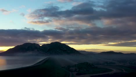 Ein-Sonnenaufgang-Langsam-3D-Aussehende-Pfanne-Mit-Bergen,-Wolken-Und-Dem-See