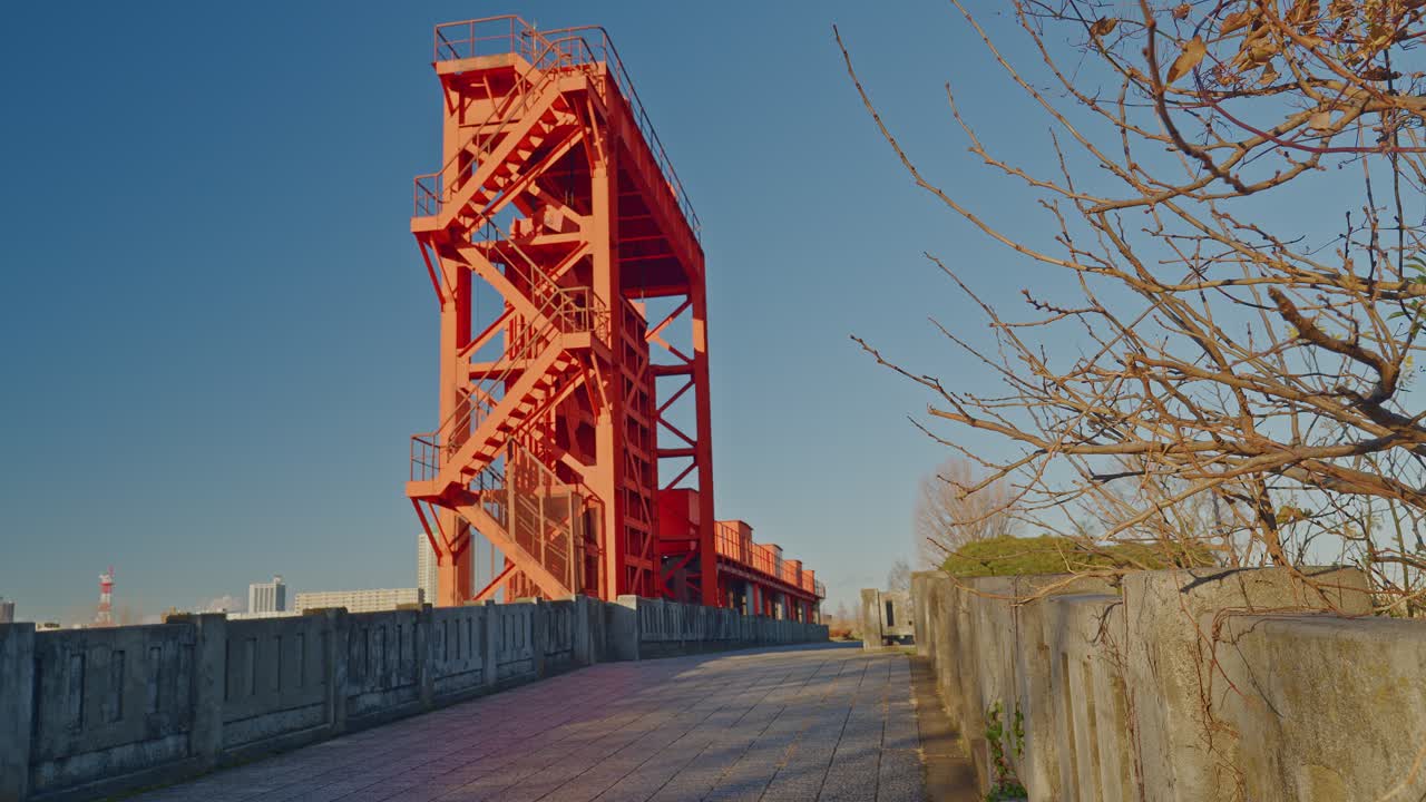 Low angle shot of the historic Red Iwabuchi Sluice Gate in Tokyo. The vibrant steel structure stands against a clear blue sky by the Arakawa River