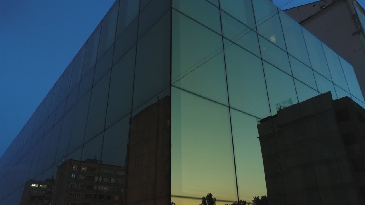 vista exterior de 4k del edificio del distrito comercial, centro comercial con ventanas de espejo de pared por la noche o por la noche. reflejo de la ciudad, la gente, los coches en las paredes espejadas. cámara de dron moviéndose. personas que trabajan dentro