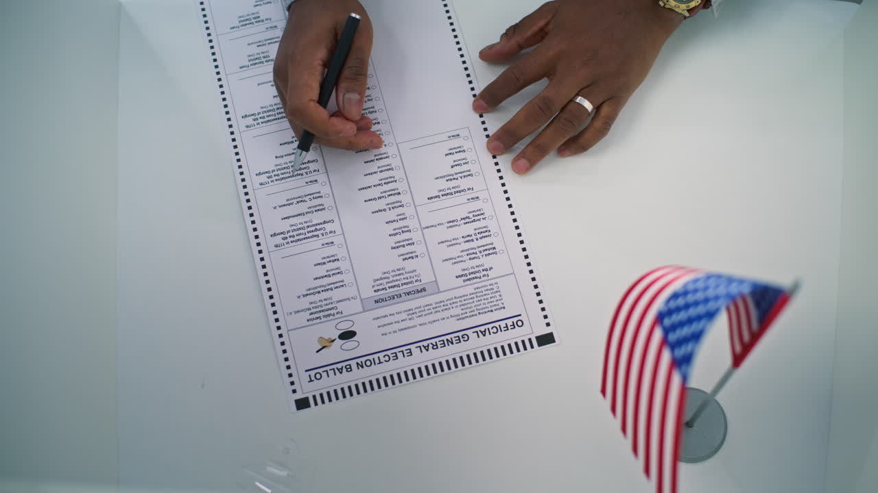 Anonymous African American Man Votes for President at Polling Place Close up of Anonymous African American Man or Businessman Filling out Paper Ballot on Table with American Flag us Citizen Votes for President at Polling Place National Election Day in United States