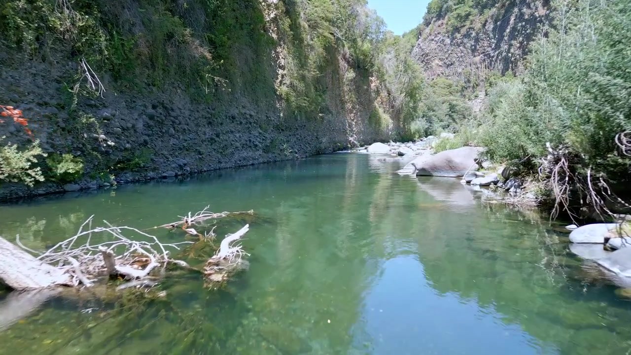 Ormanlık dağ yamaçları üzerinde ağaç tepelerine değerek, derin bir vadi ve ufuk boyunca uzanan And Dağları zirveleri ile engebeli kayalık bir zirveye doğru alçak bir uçuş. El Radal, Şili.