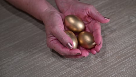 elderly female hands reveal three golden nest eggs for retirement and wealth planning