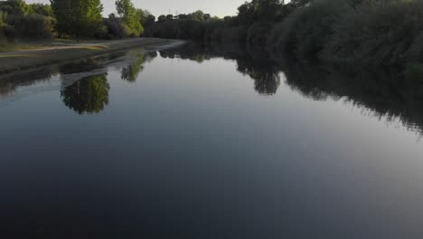 drone shot of a calm river surrounded by trees during sunset