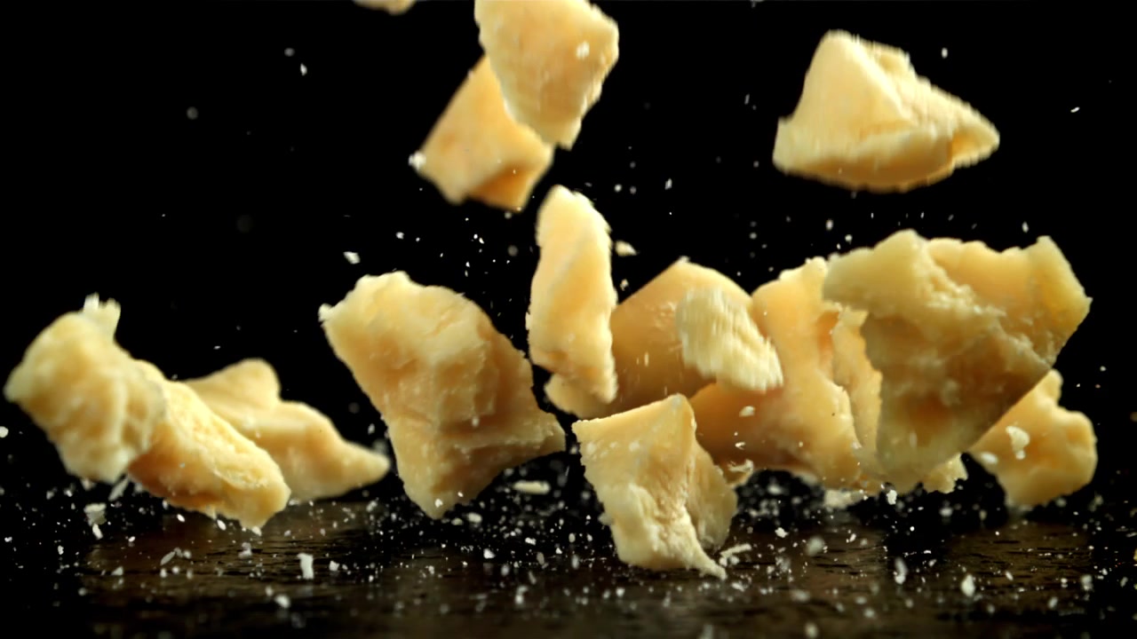 Parmesan Cheese Pieces Falling and Scattering on Black Background in Slow Motion