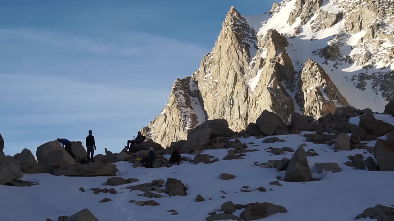 Pan of hikers taking a break with the sun hitting the mountains in the background.