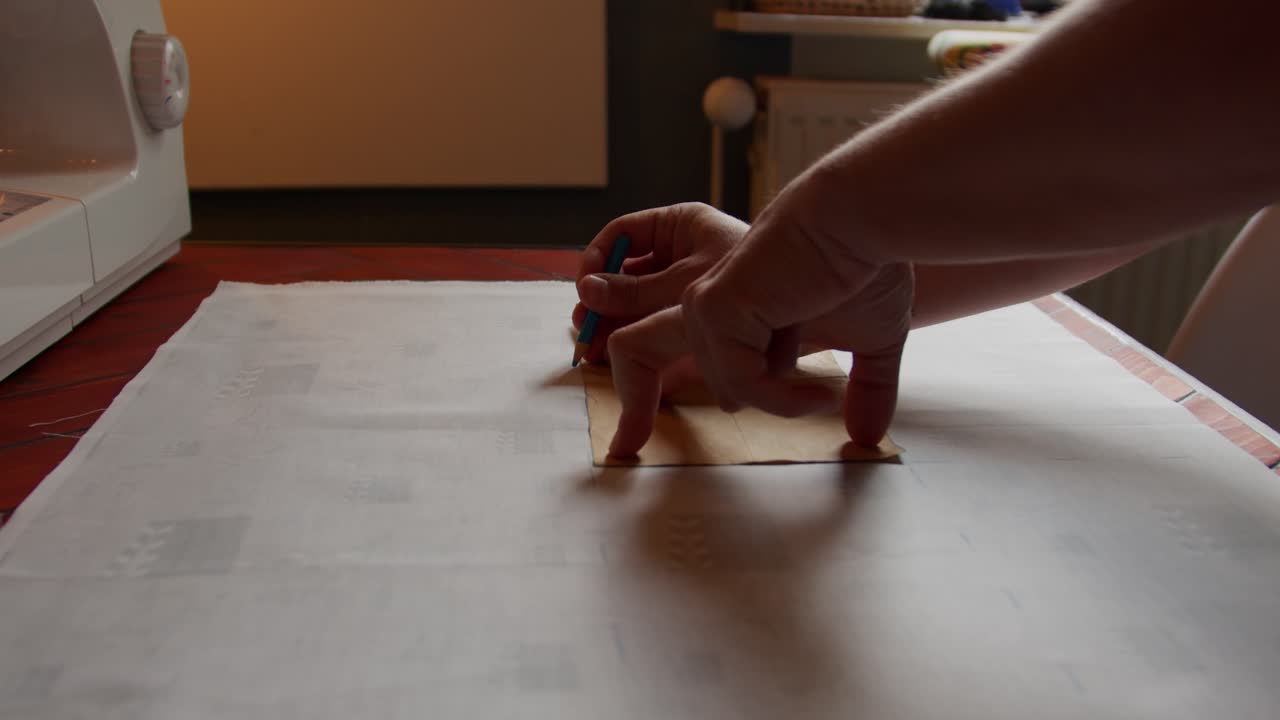 Backward motion shot as hands mark on fabric using a pattern on a work surface.
