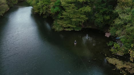 Texas-Flyfisherman-Lanza-Caña-De-Pescar-Mientras-Vadea-En-Un-Hermoso-Río-Con-Un-Paisaje-De-árboles-Exuberantes-Cerca-De-La-Costa,-Orbitando-Un-Dron-Aéreo-Giratorio-En-4k