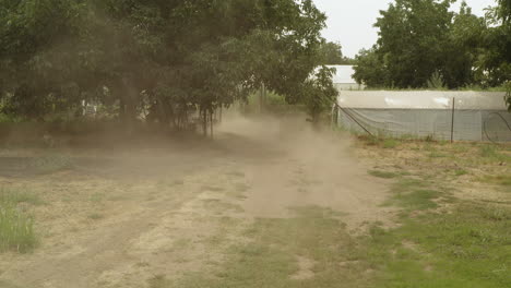 an atv towing a trailer through a dirt field in a farm and lifting up dust