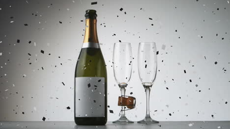 confeti cayendo sobre una botella de champán y dos vasos de champán contra un fondo gris