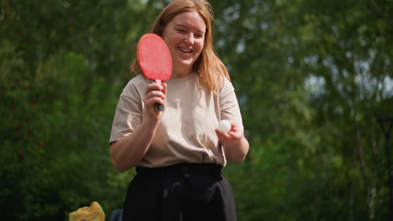 Mujer disfrutando de una actividad de ocio al aire libre, mujer equilibrando con soltura pala y pelota en un entorno natural, mujer serena haciendo malabares con confianza con pala y pelota en un tranquilo entorno verde al aire libre