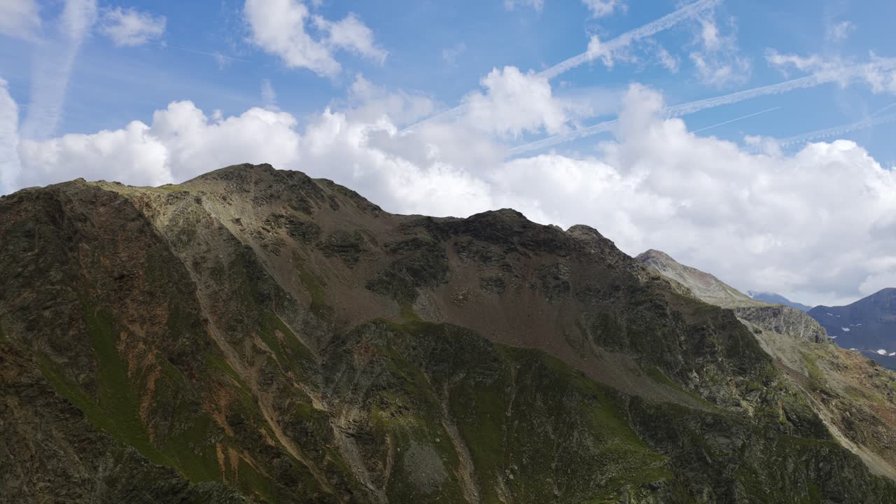 Rugged mountain landscape at Umbrail Pass. Shows barren rocky peaks and green slopes under blue sky with clouds. For nature or travel content, Swiss Alps, Switzerland