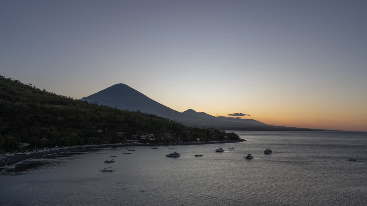 Sunset over a tropical bay with boats and volcanoes